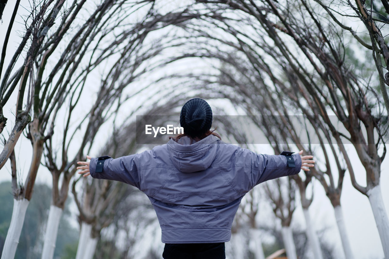 Rear view of woman with arms outstretched standing against trees