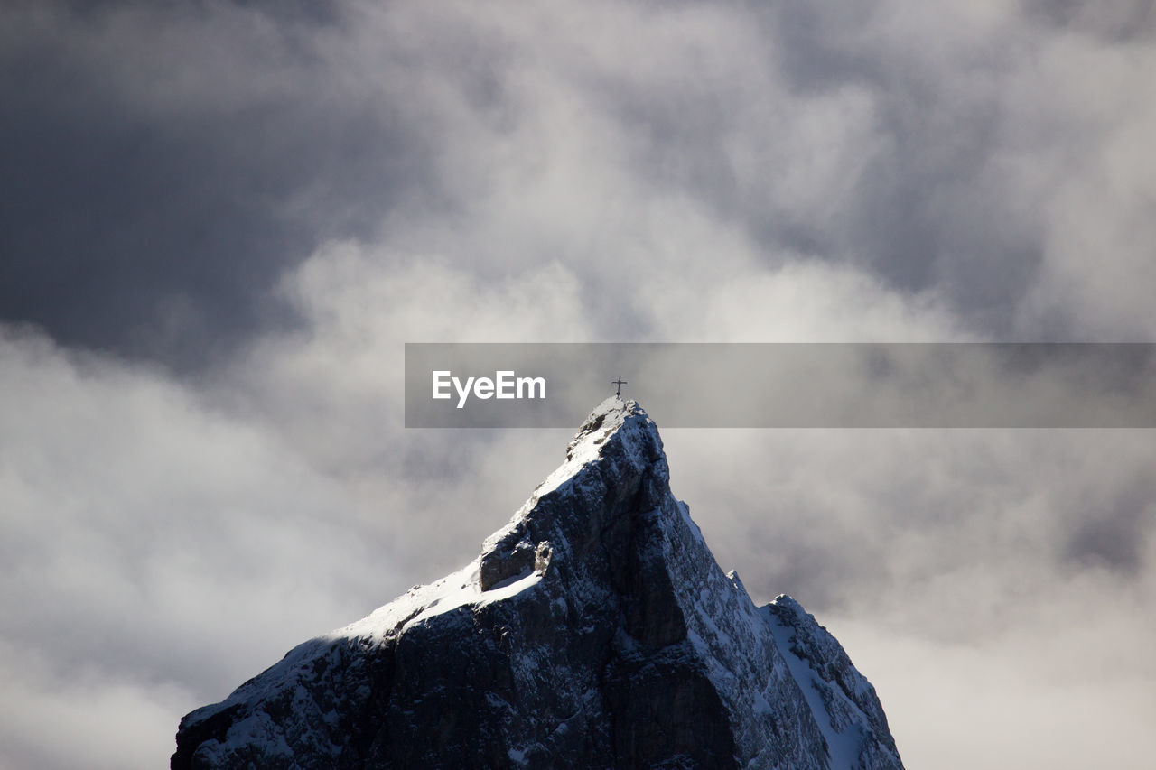 Dramatic view of mountain peak with summit cross against stormy clouds