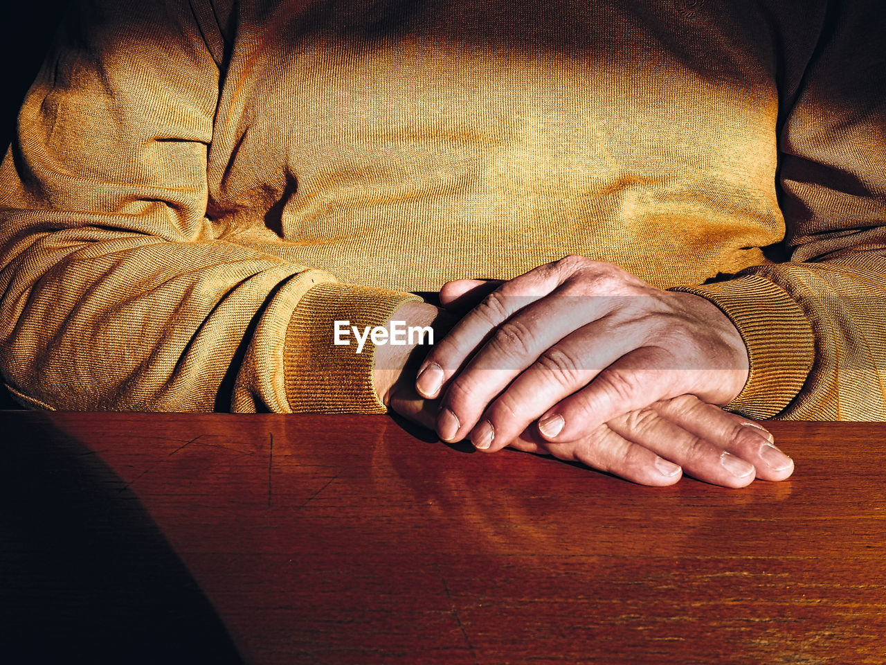 Midsection of man with hands clasped sitting at table