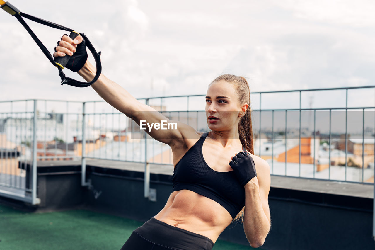 Woman exercising against cloudy sky