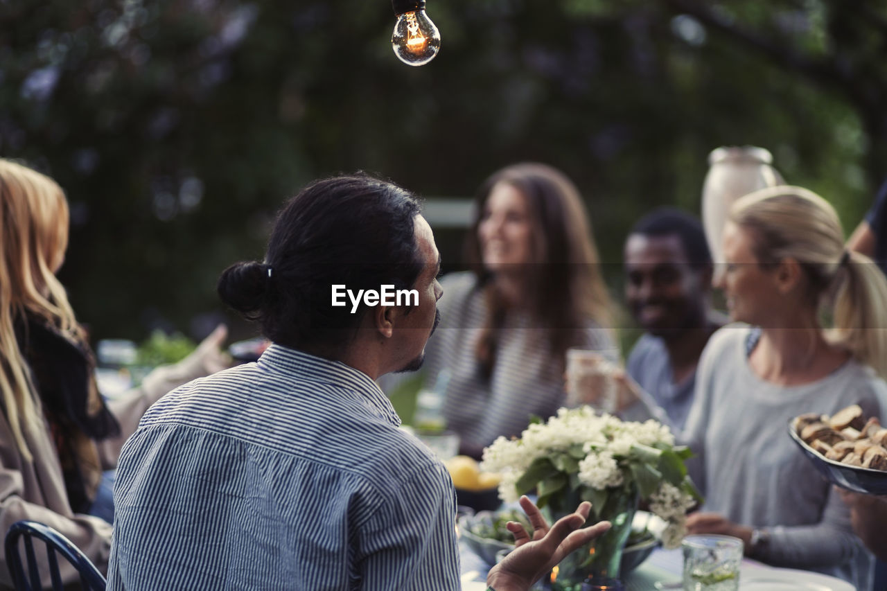 Rear view of man sitting at dining table with friends at outdoor dinner party