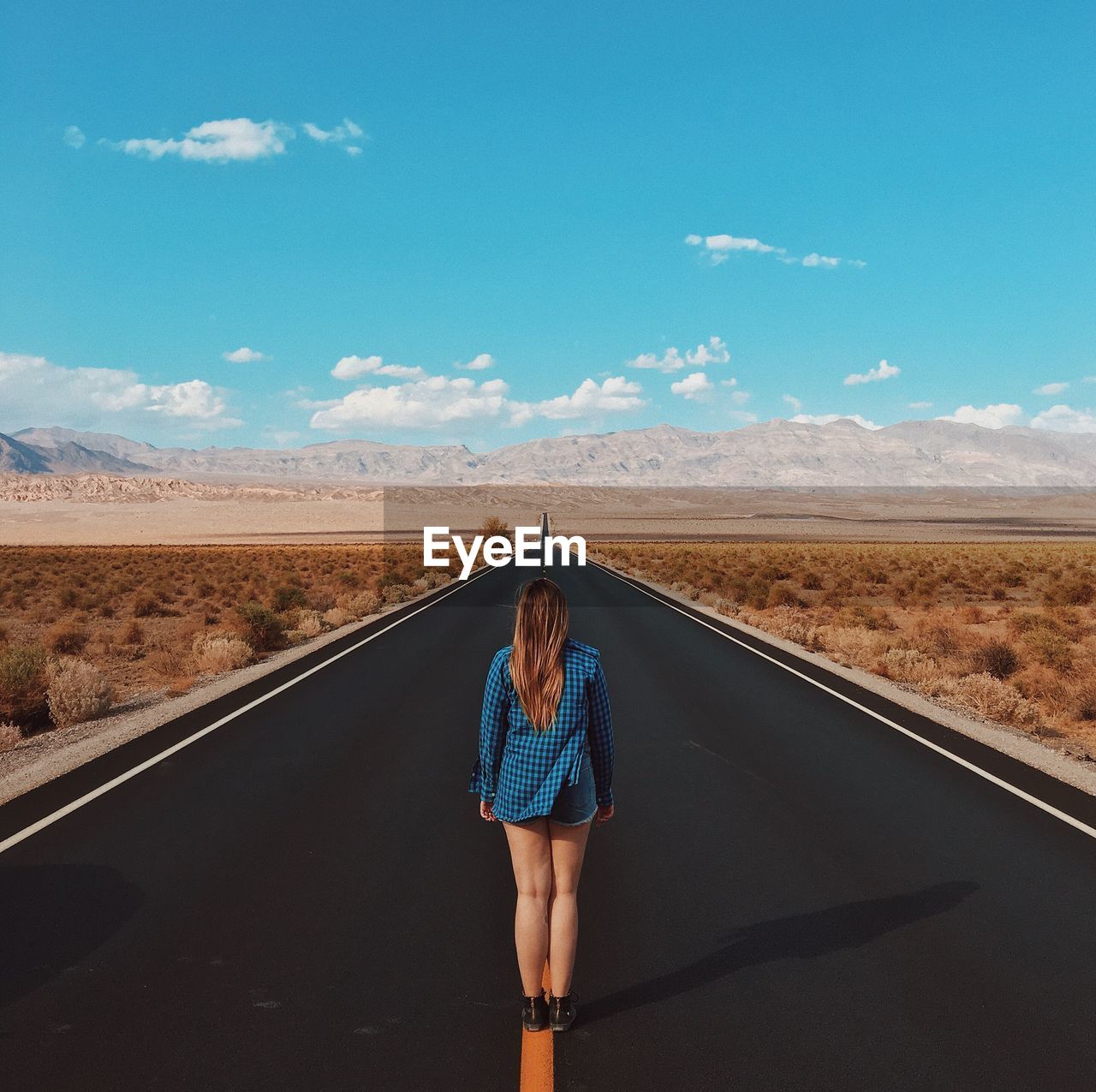 Rear view of girl standing on road against blue sky