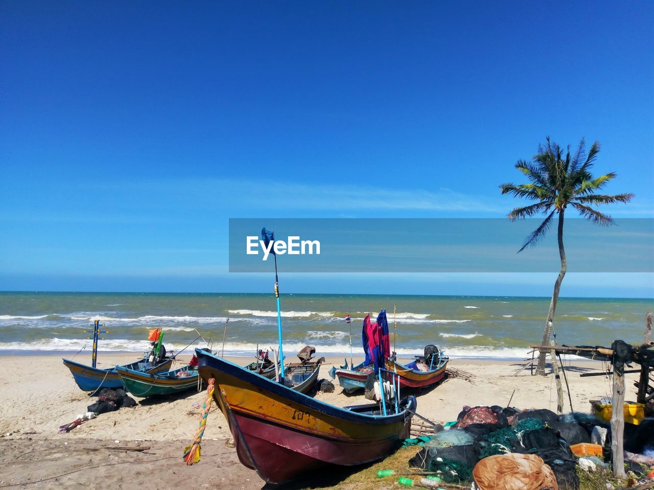 Boats moored on beach against blue sky