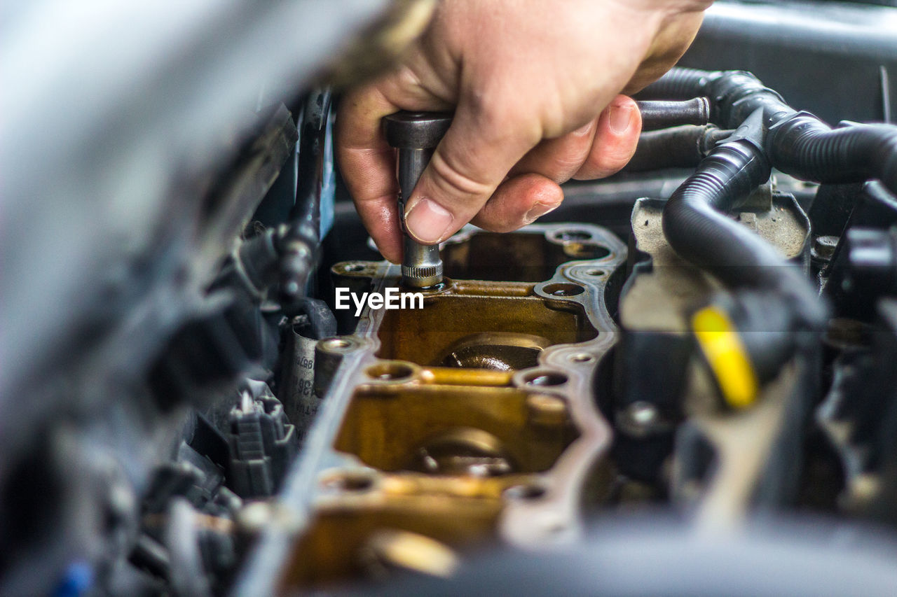 hand, selective focus, occupation, adult, vehicle, one person, working, technician, mechanic, technology, close-up, transportation, focus on background, work tool, mode of transportation, men, indoors, equipment, industry, motor vehicle, engine, holding, business finance and industry, wheel, business, service, car, skill