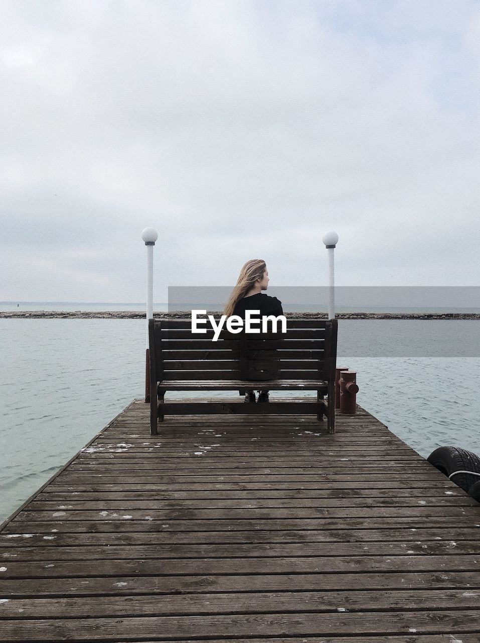 Rear view of man sitting on pier over sea against cloudy sky