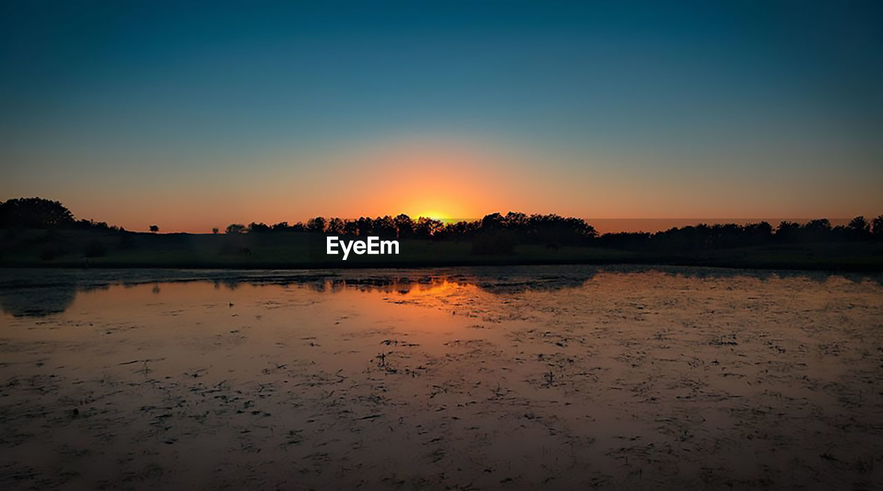 Scenic view of lake against clear sky during sunset