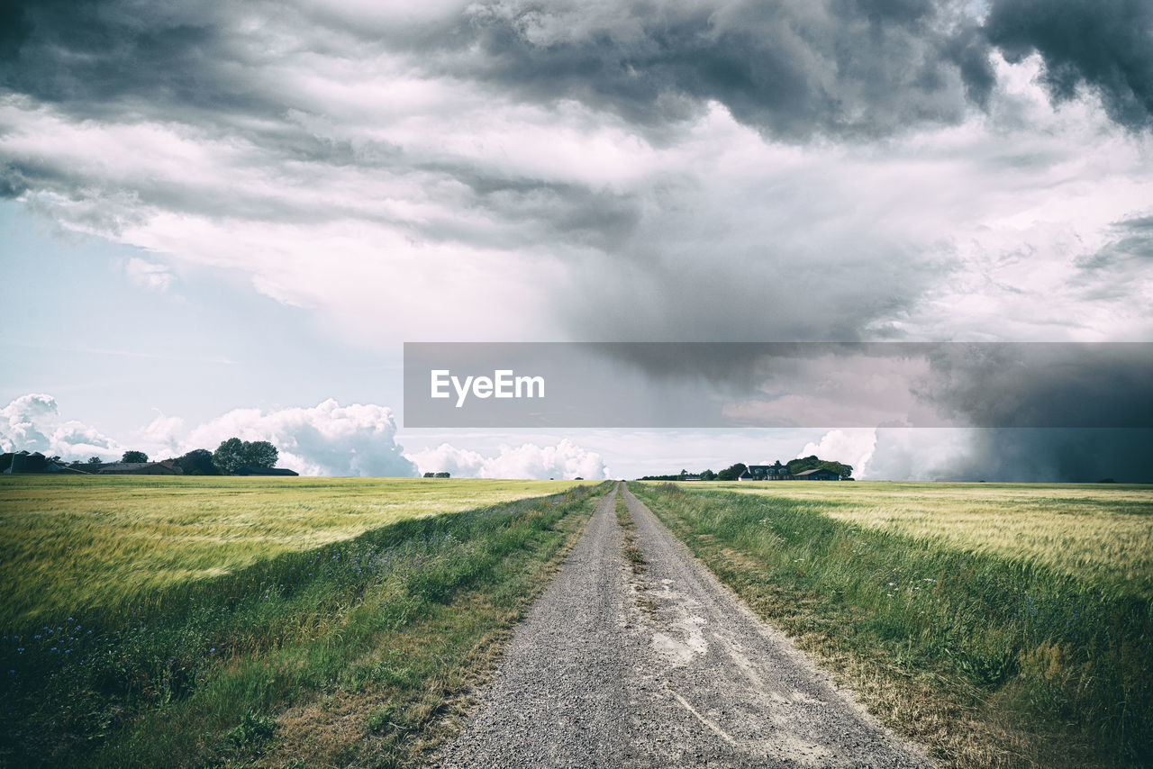 Empty road amidst field against sky