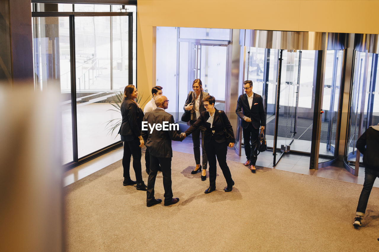 Colleagues looking at business professionals shaking hands in office lobby