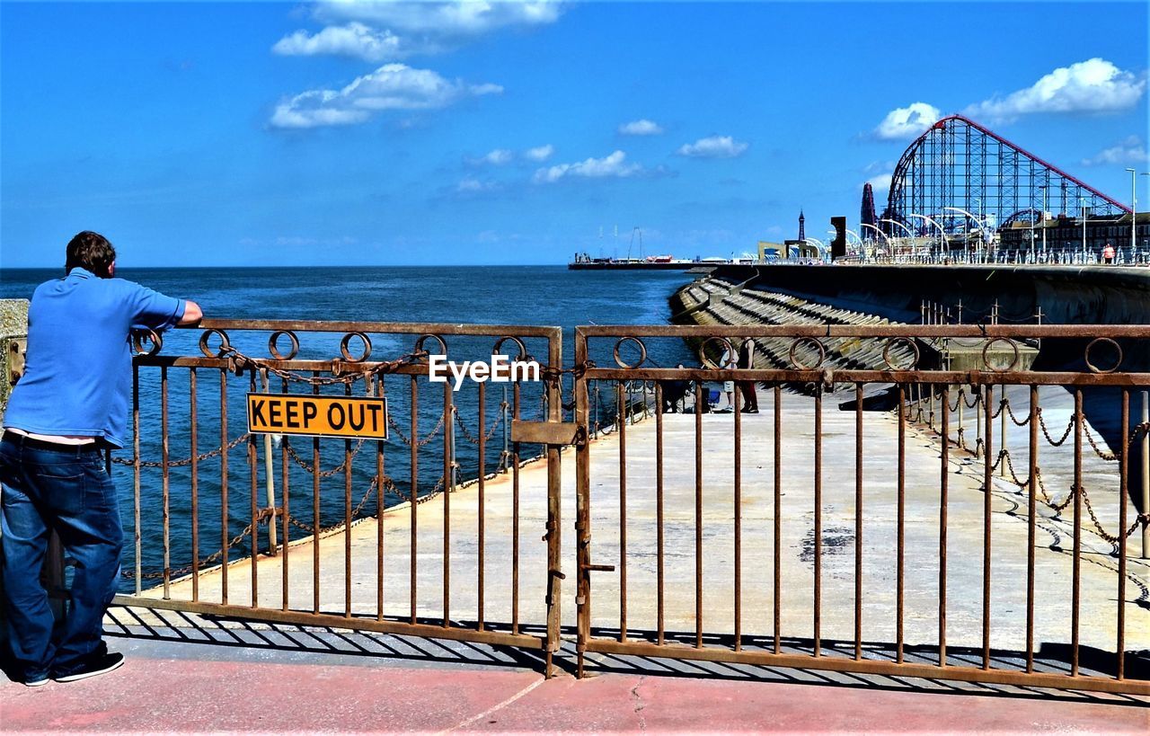 Rear view of man standing by railing against sea