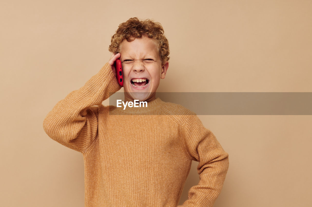 Boy talking on phone against beige backgrounds