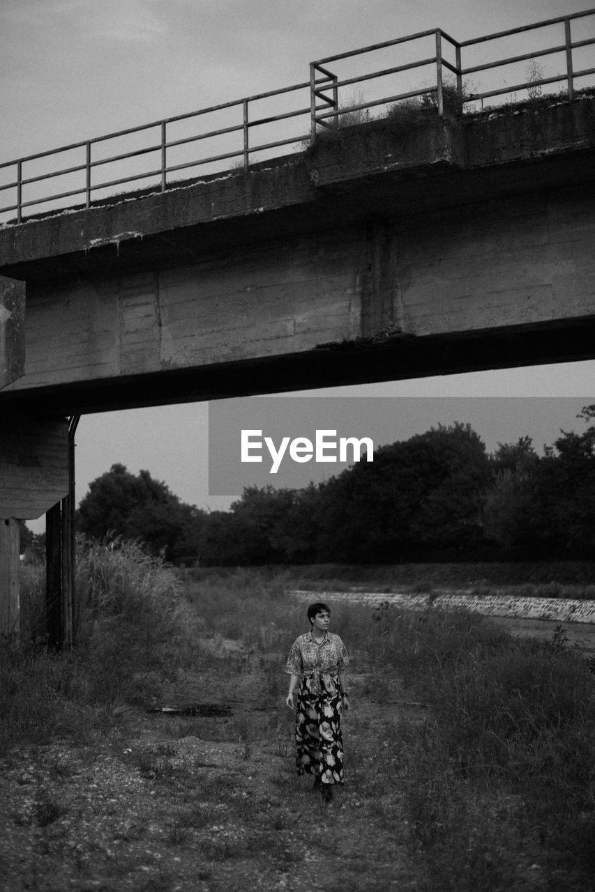 Rear view of woman  walking under bridge against sky