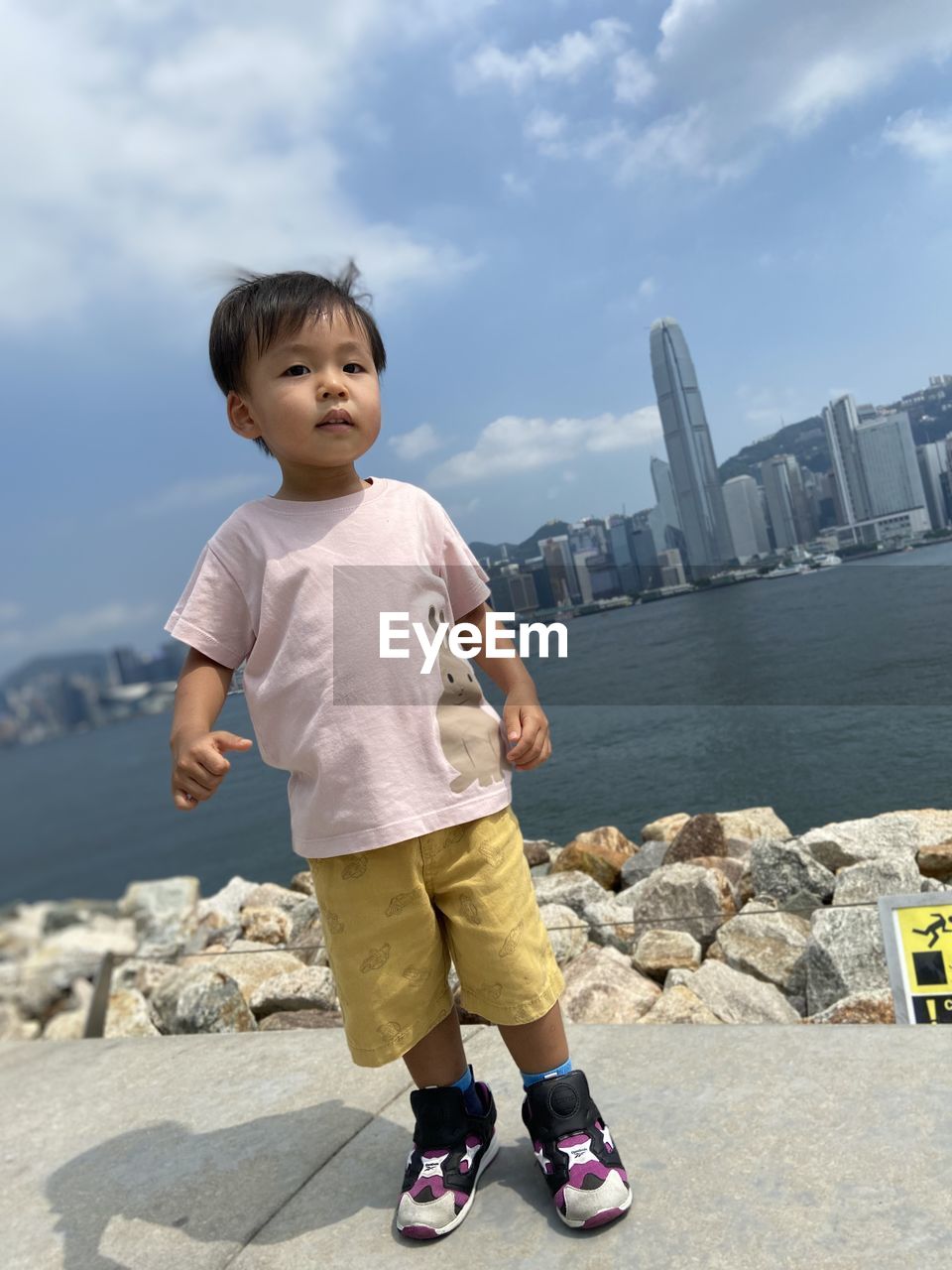 Side view of asian cute boy standing at harbour against sky