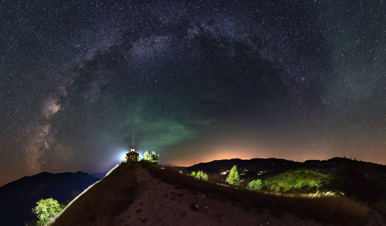 Distant view of illuminated chapel on mountain against star field
