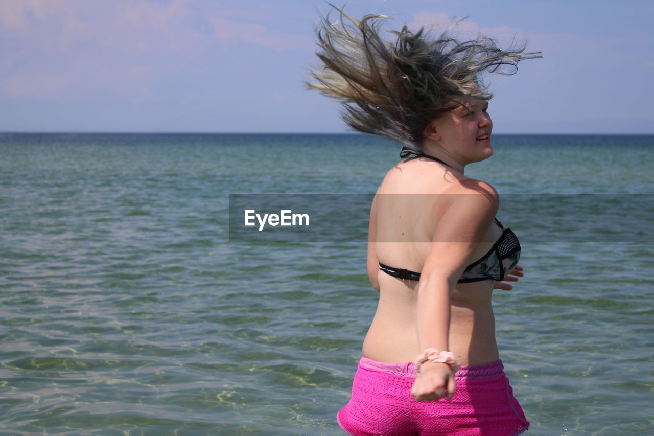 BEAUTIFUL YOUNG WOMAN STANDING IN SEA AGAINST SKY