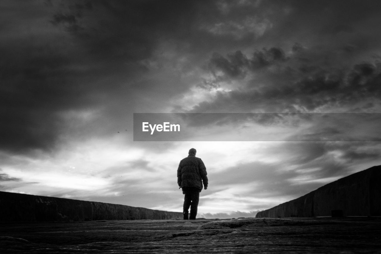 FULL LENGTH REAR VIEW OF MAN WALKING ON FIELD AGAINST SKY