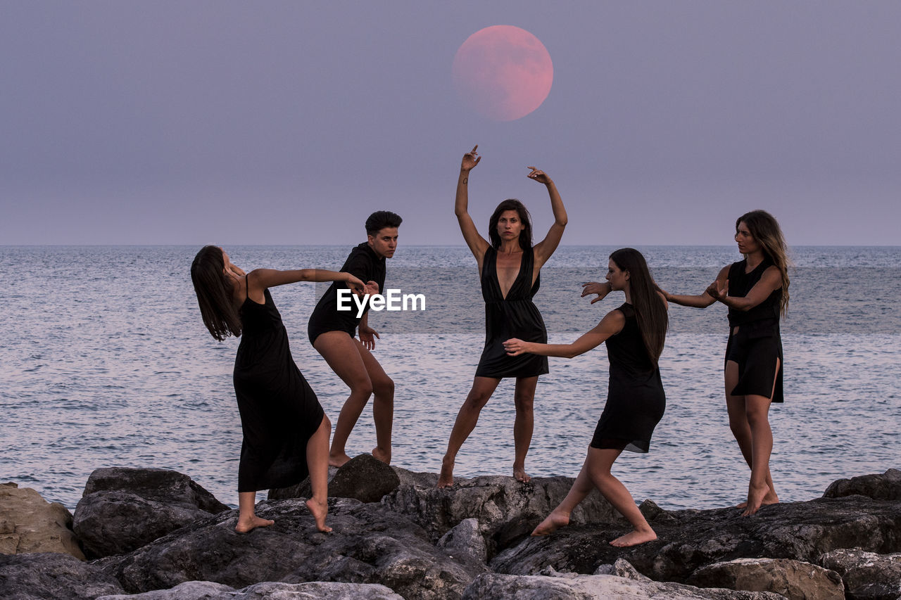 Fashion models posing on rocks by sea against sky