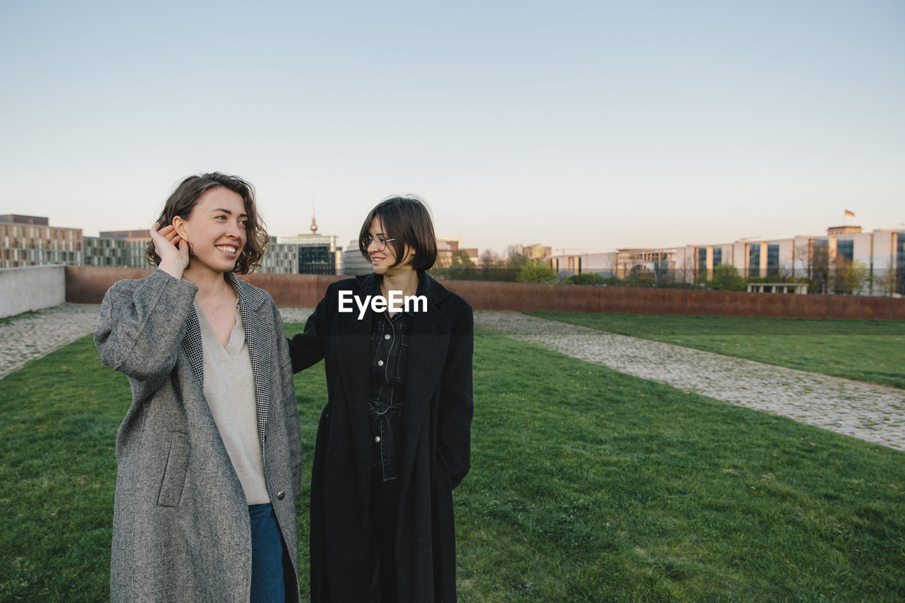 Smiling lesbian couple walking in park against clear sky