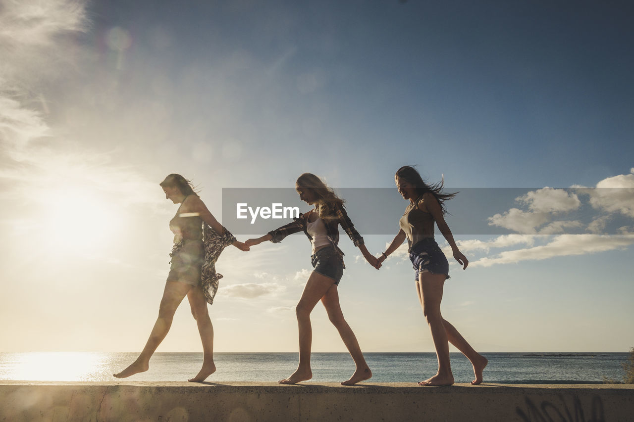 Low angle view of friends walking against sea