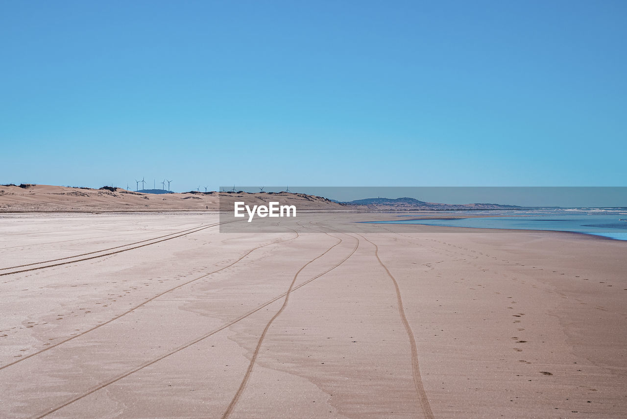 Tyre track and footprints mark on sand with seascape and blue sky