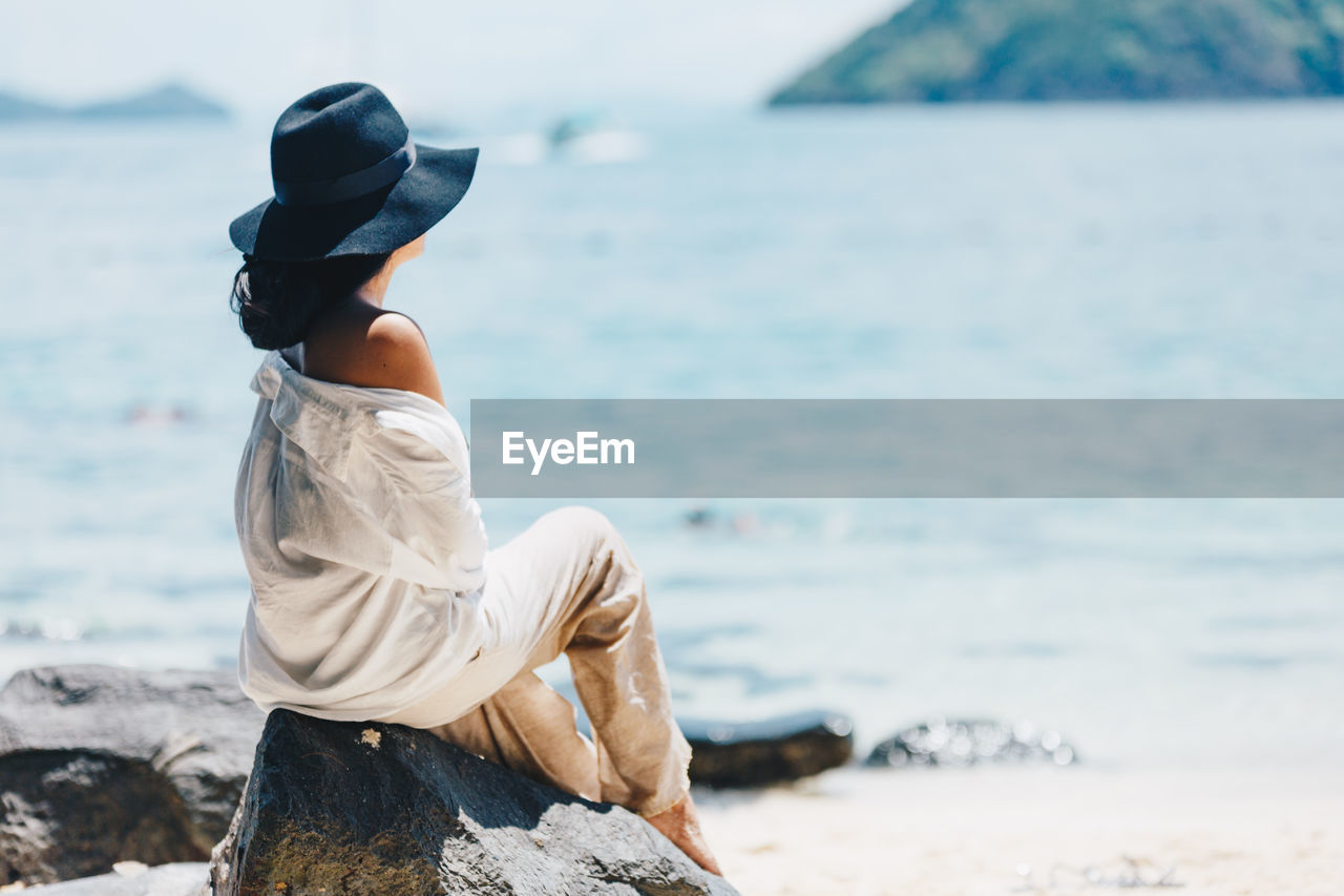 Rear view of woman relaxing on rock at beach