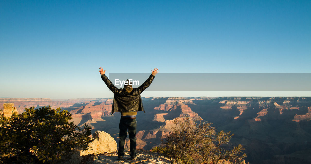 Rear view of person standing next to mountains against clear sky