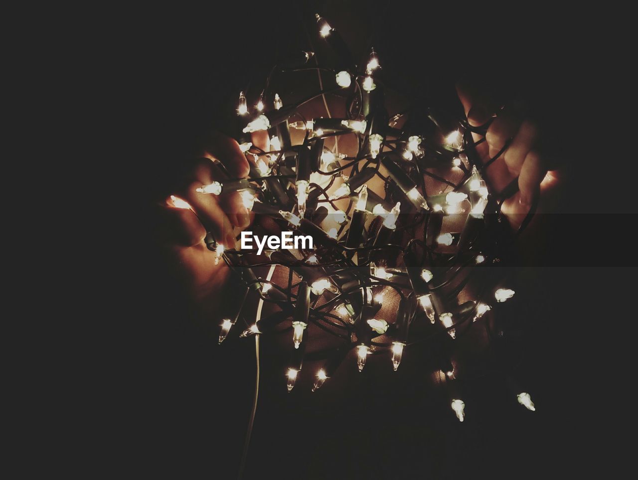 Close-up of hands holding illuminated string lights in darkroom