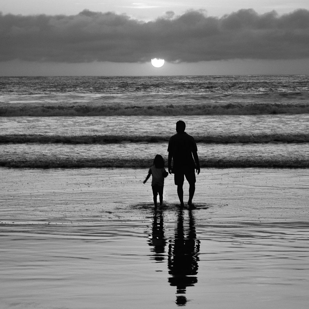 Father and daughter in sea at sunset