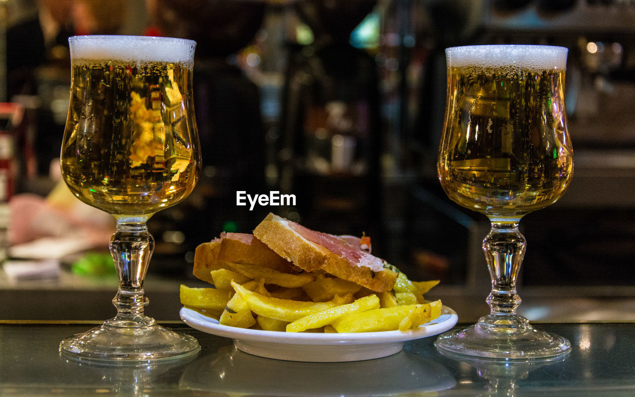 Close-up of beer glasses with french fries and bread on table