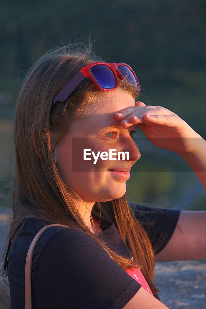 Close-up of smiling woman with shielding eyes looking away