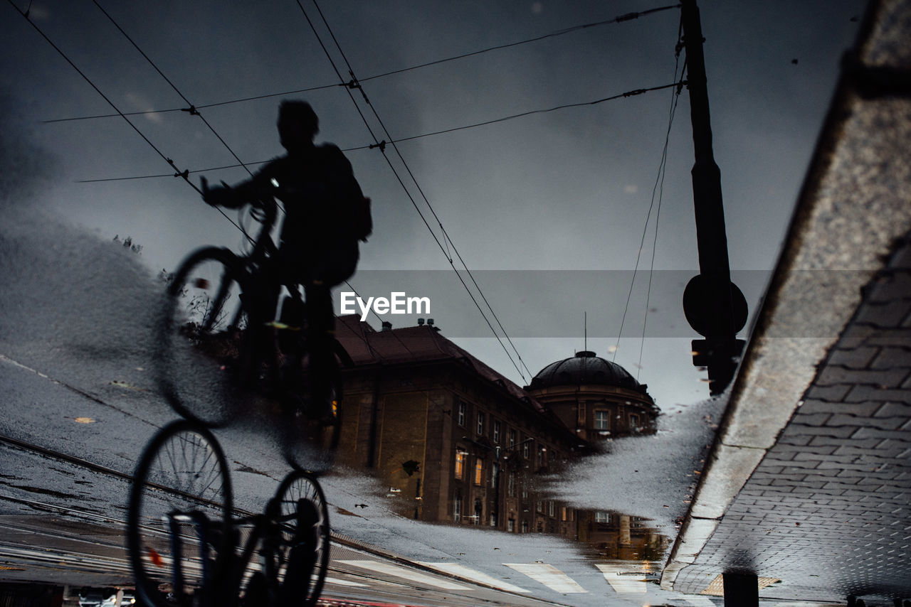 Reflection of silhouette man riding bicycle in puddle on road