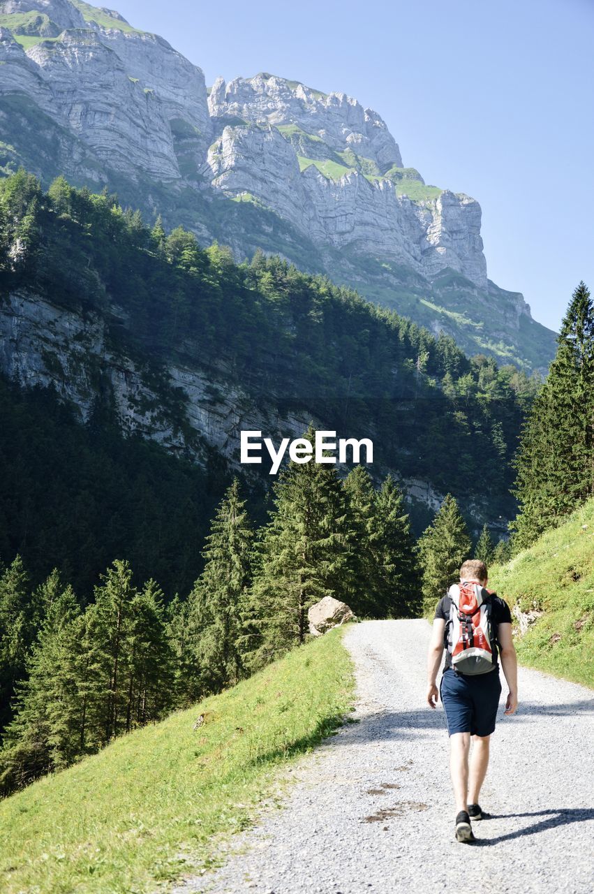 Rear view of man with backpack walking on road