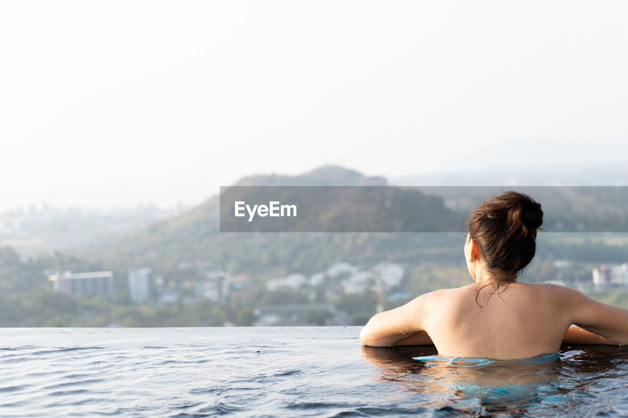Rear view of woman in infinity pool against clear sky