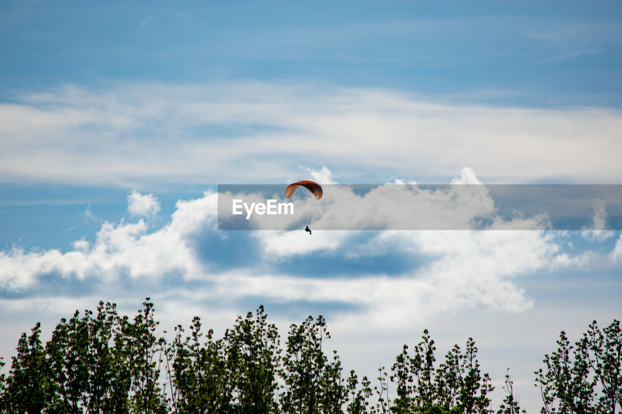 Mid distance view of person paragliding against cloudy sky