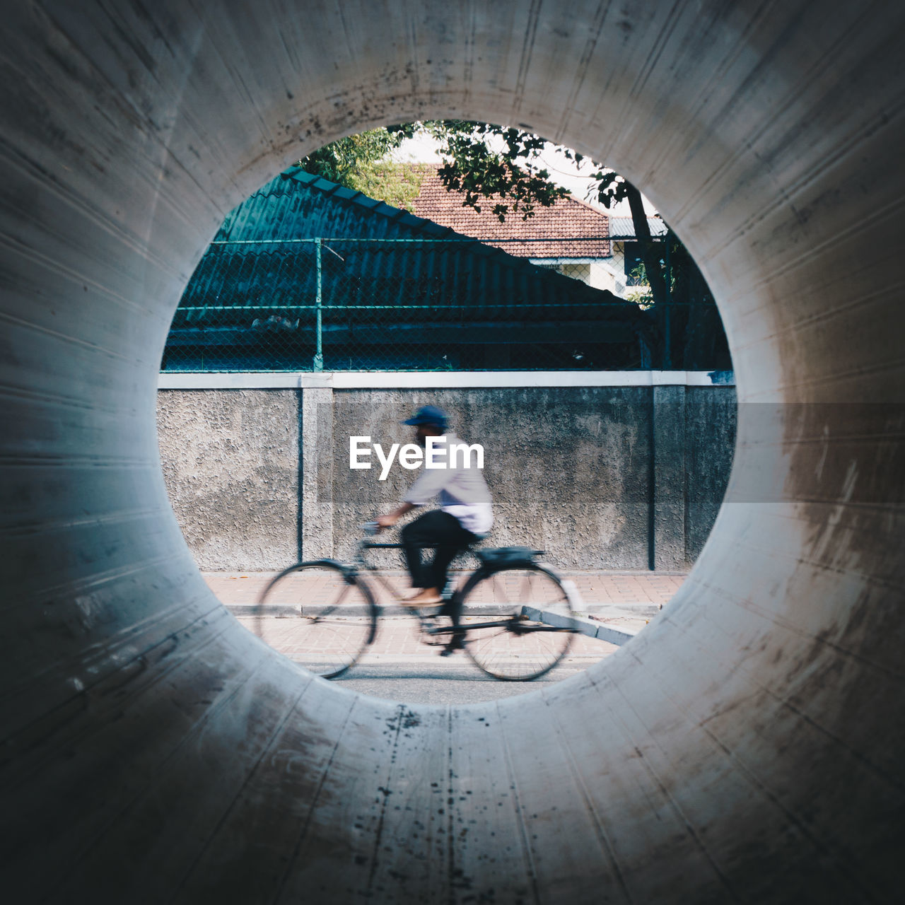 Blurred motion of man riding bicycle seen through concrete pipe hole