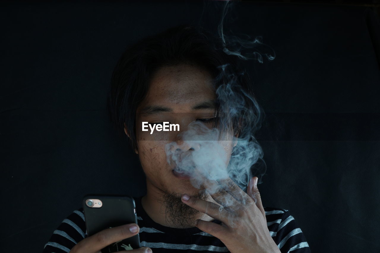 Close-up of young man smoking cigarette against wall