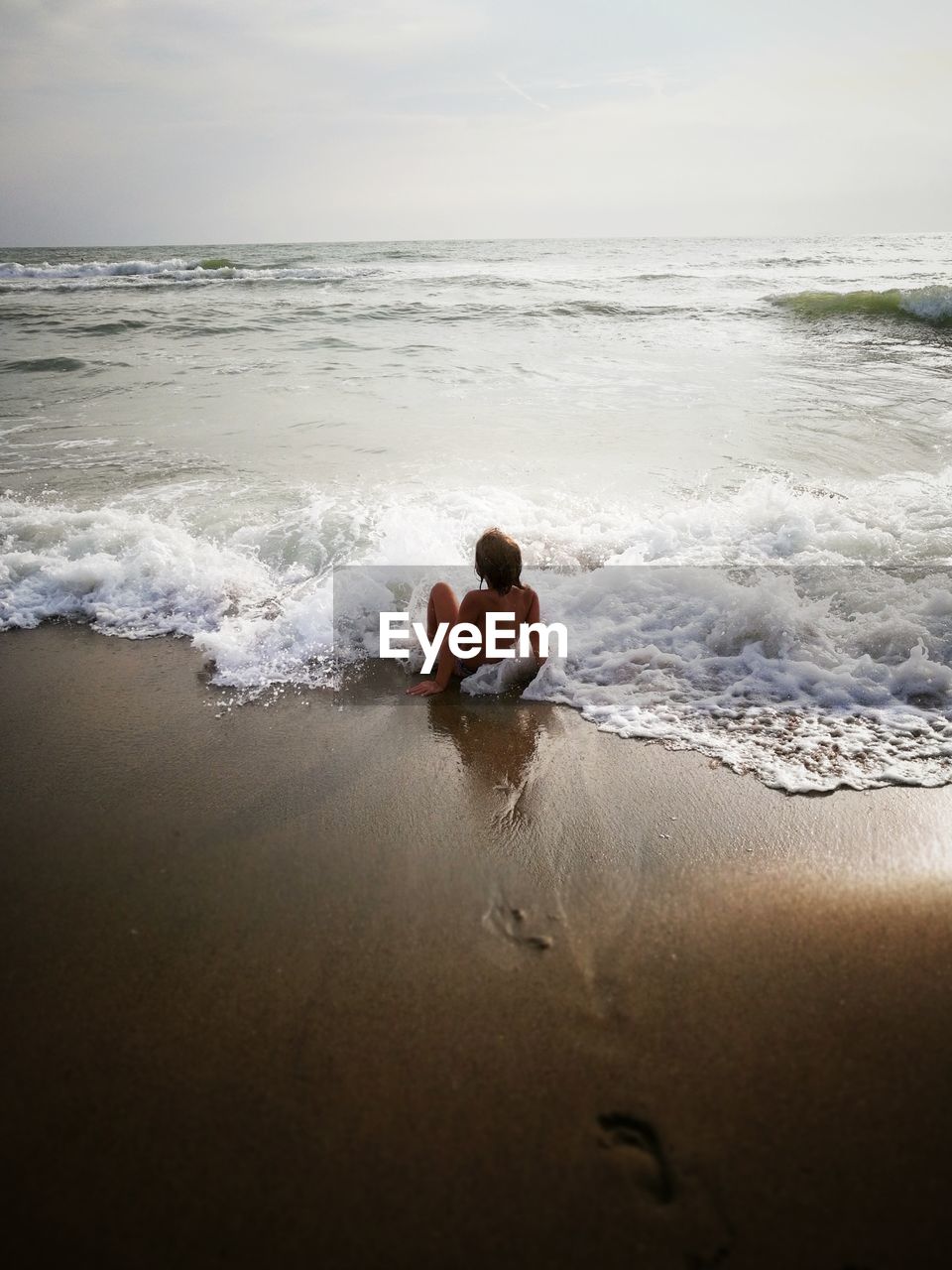 Rear view of shirtless boy sitting at sea against sky