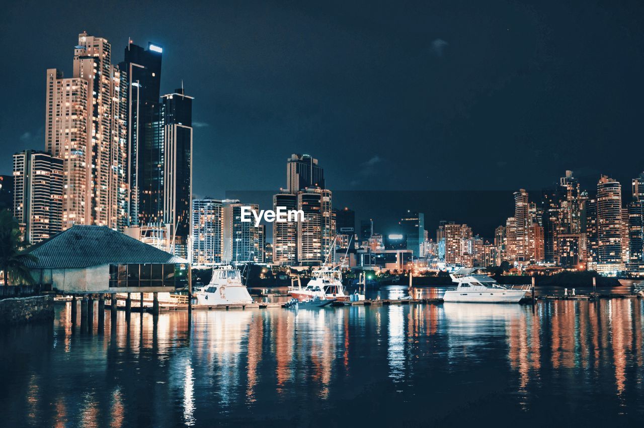 Illuminated buildings by river against sky at night in panama