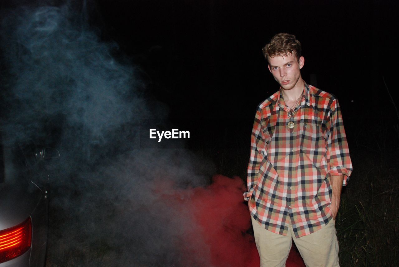 Young man standing by smoke on field at night