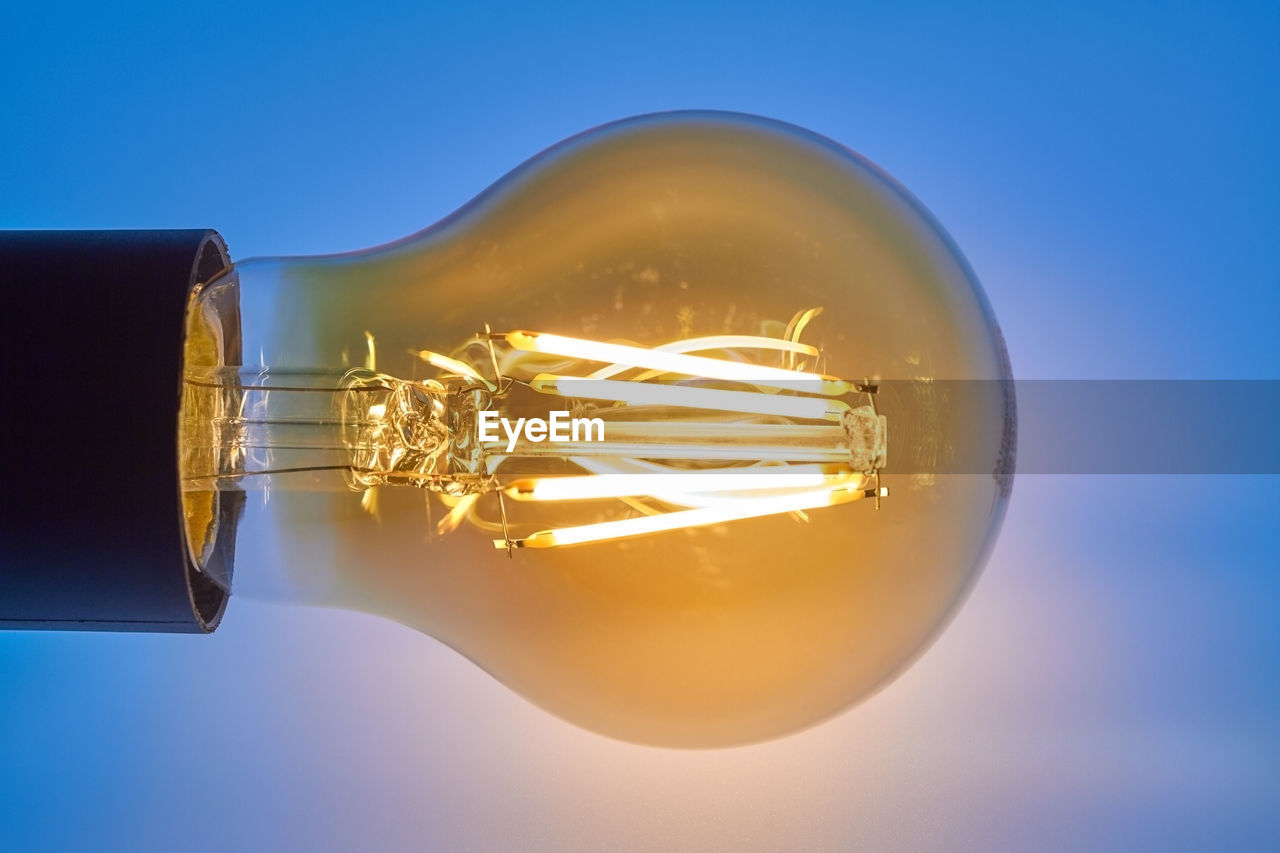 Close-up of illuminated light bulb against blue background