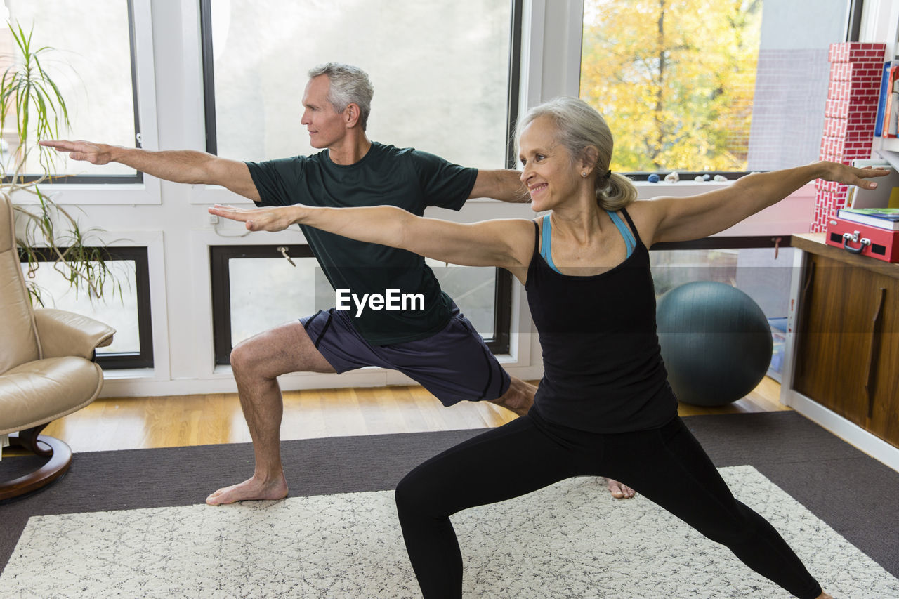 Couple with arms outstretched and legs apart exercising at home