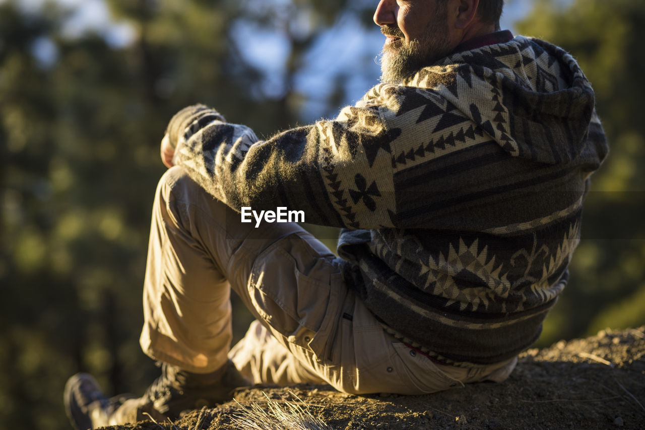 REAR VIEW OF MAN SITTING ON ROCK