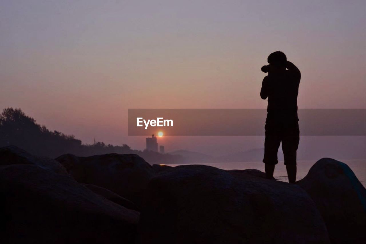 SILHOUETTE MAN STANDING ON ROCK DURING SUNSET