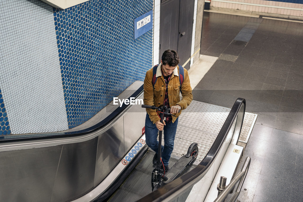 Man in stylish outfit with electric scooter in the mechanic stair of underground