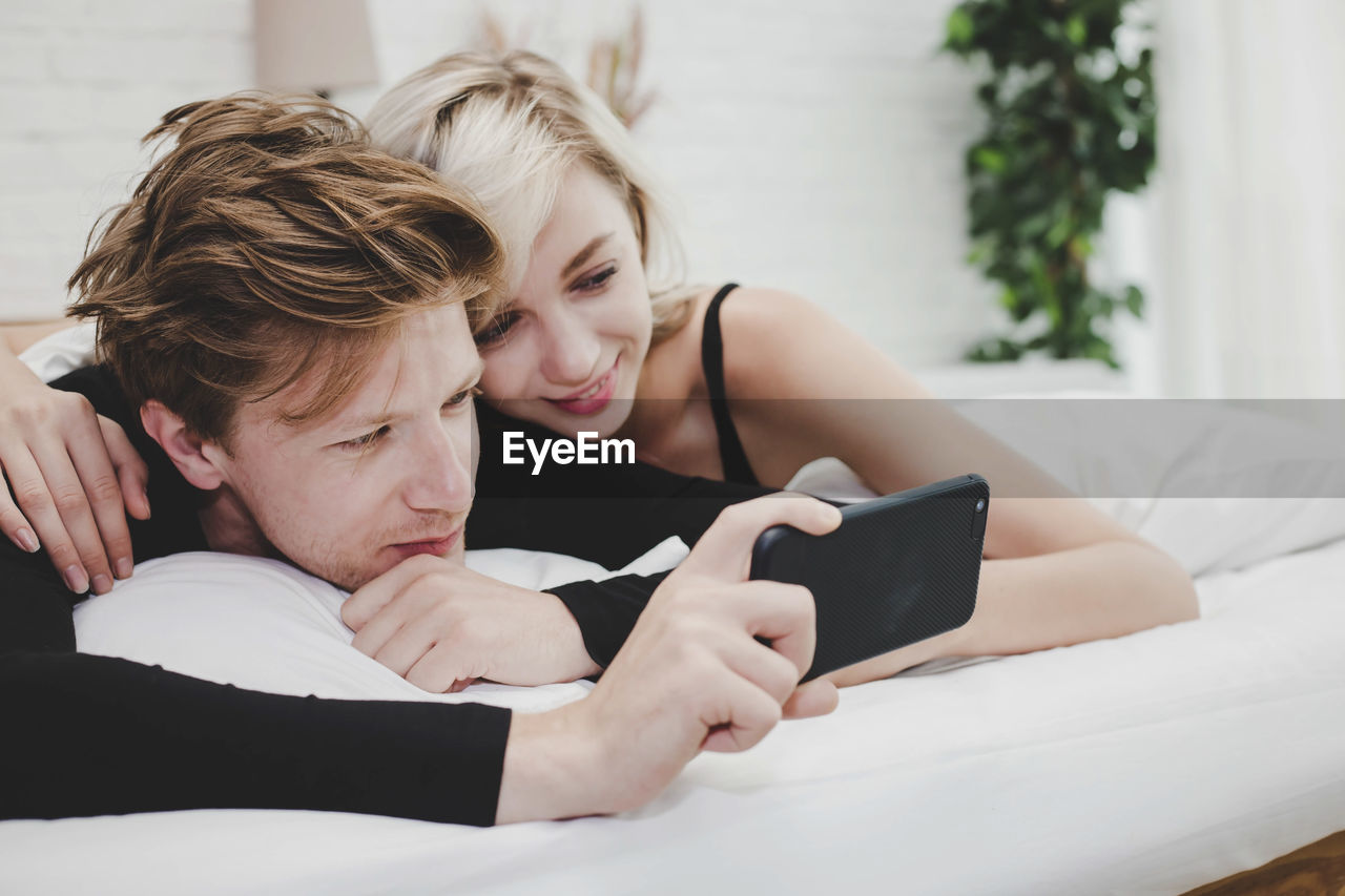 Close-up of couple watching video on mobile phone while lying on bed