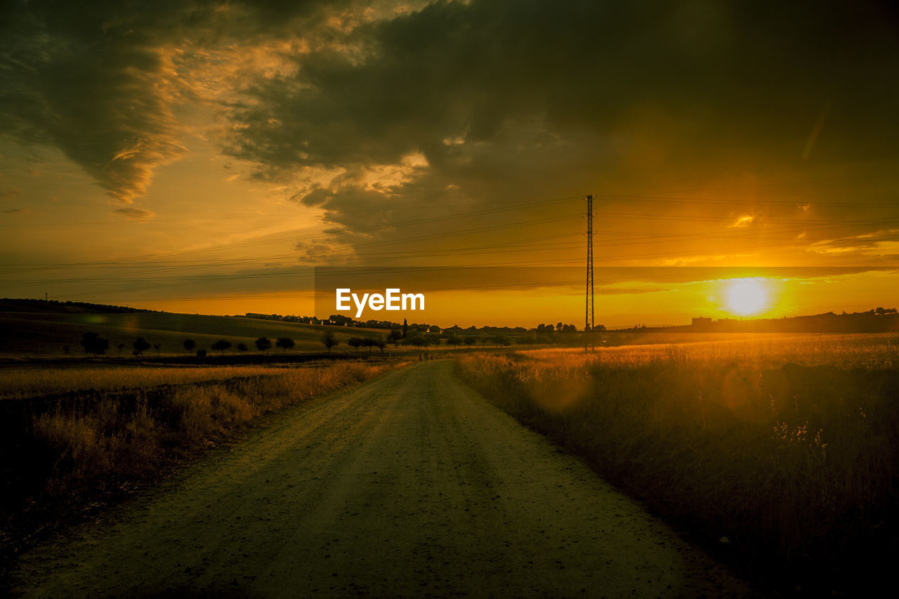 Road amidst agricultural field against sky during sunset