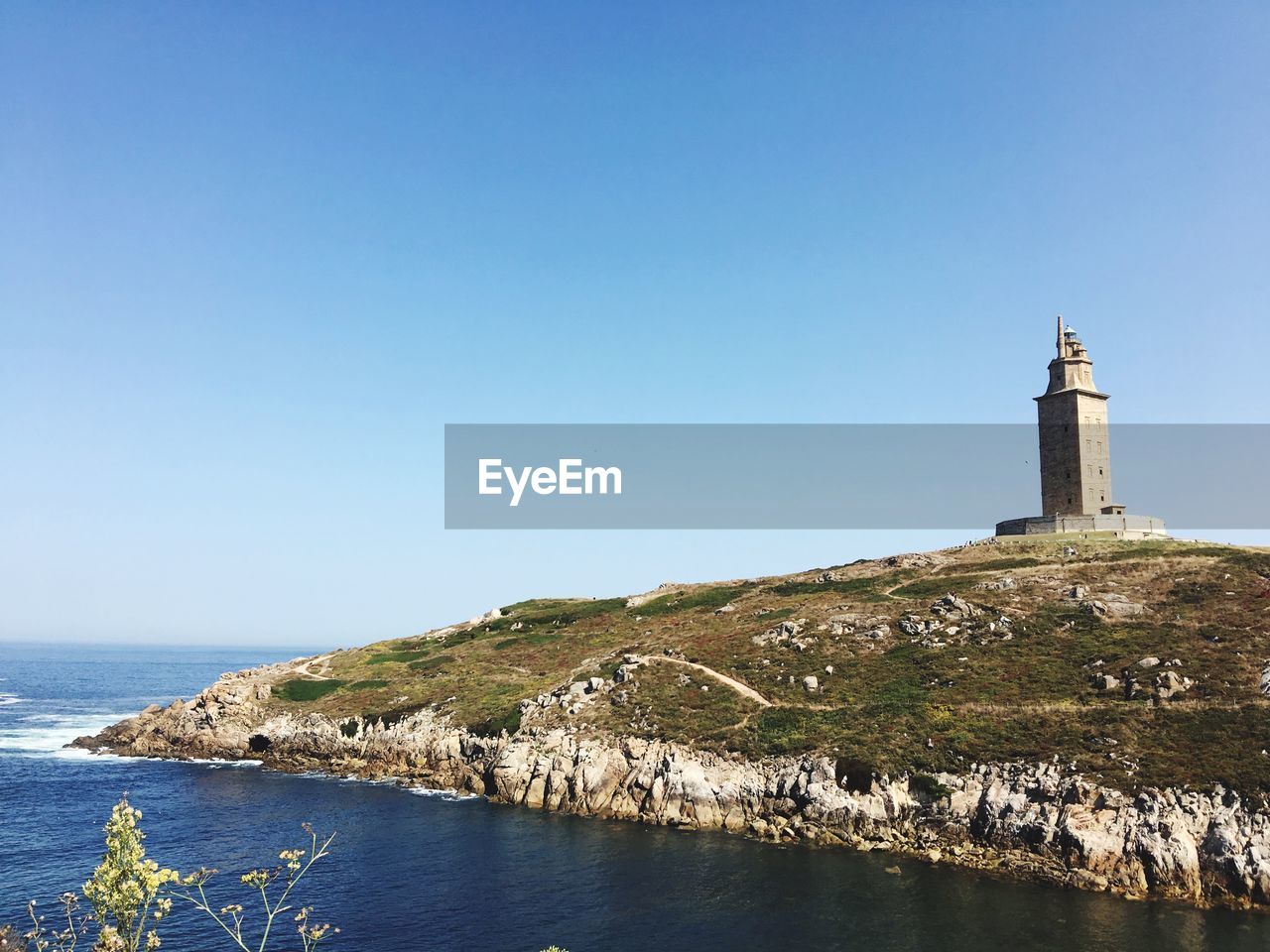 Lighthouse by sea against clear sky