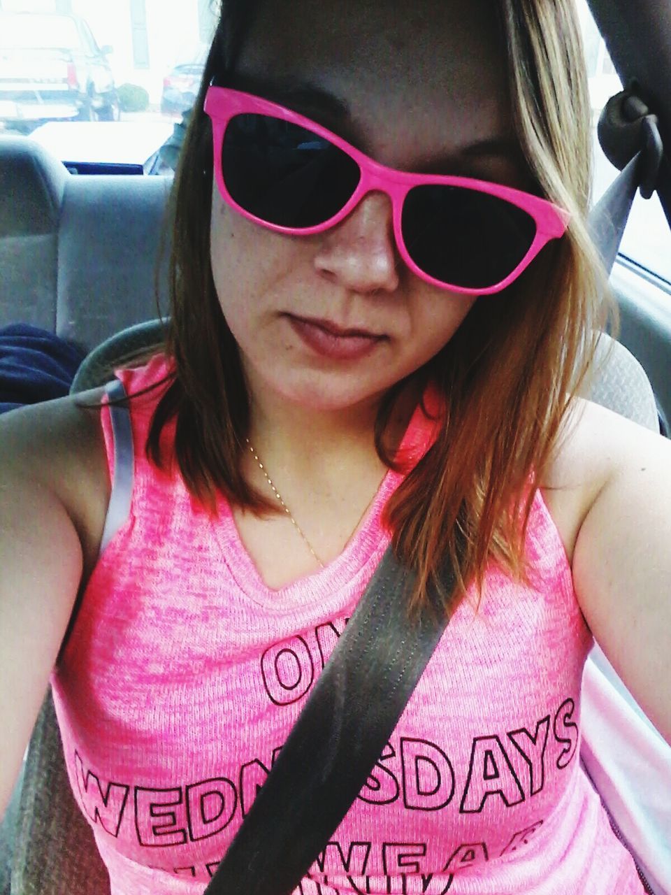 Woman wearing pink sunglasses and top sitting in car