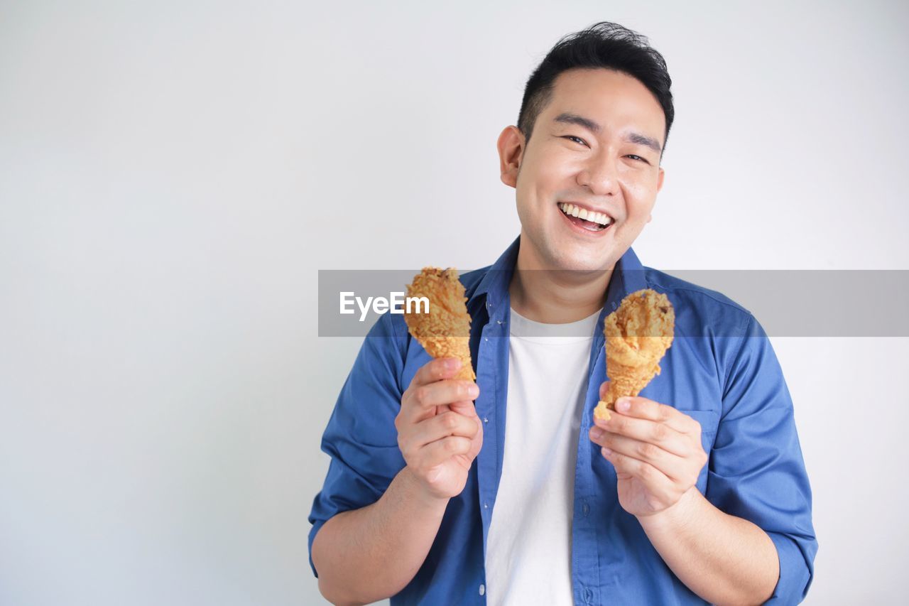 Happy asian man holding fried chicken bucket standing over white background with copy space.