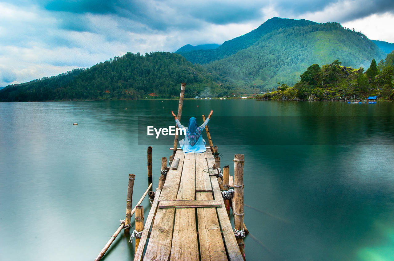 Woman sitting on pier over lake