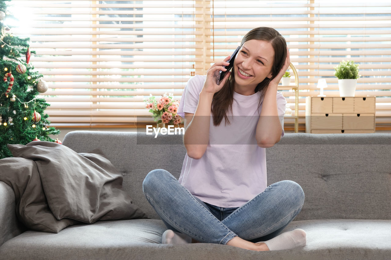 portrait of young woman using mobile phone while sitting on sofa at home